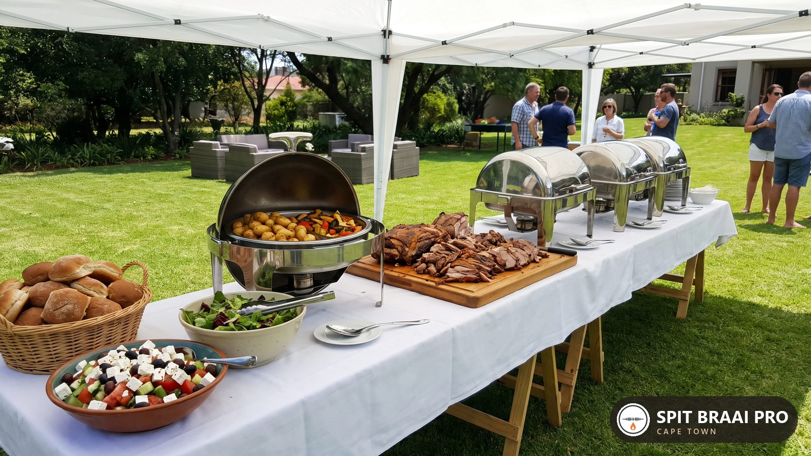 Carved spit-roast meat and side dishes laid out on an outdoor catering table